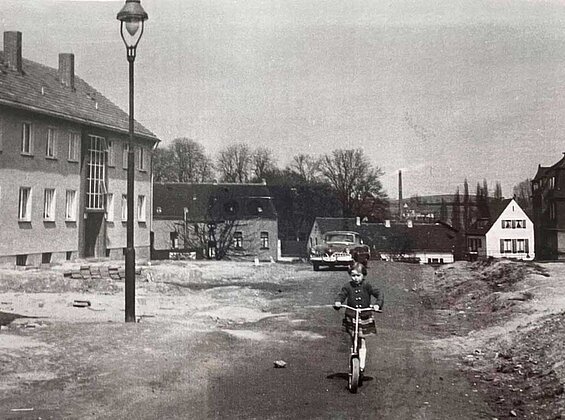 Kind in einer Siedlung mit einem Tretroller. Historische Aufnahme aus Erkrath.