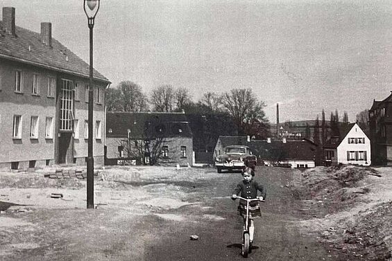 Kind in einer Siedlung mit einem Tretroller. Historische Aufnahme aus Erkrath.